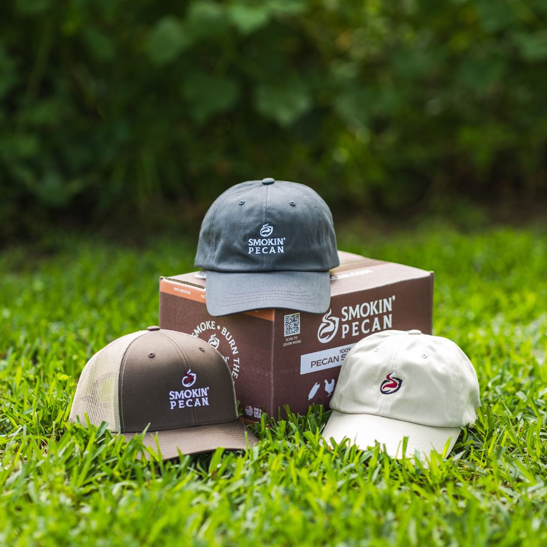 Three caps and a box of Smokin' Pecan products on grass