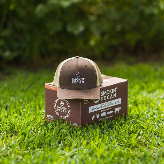Brown cap with 'Smokin' Pecan' logo on a box of pecan shell pellets in grass